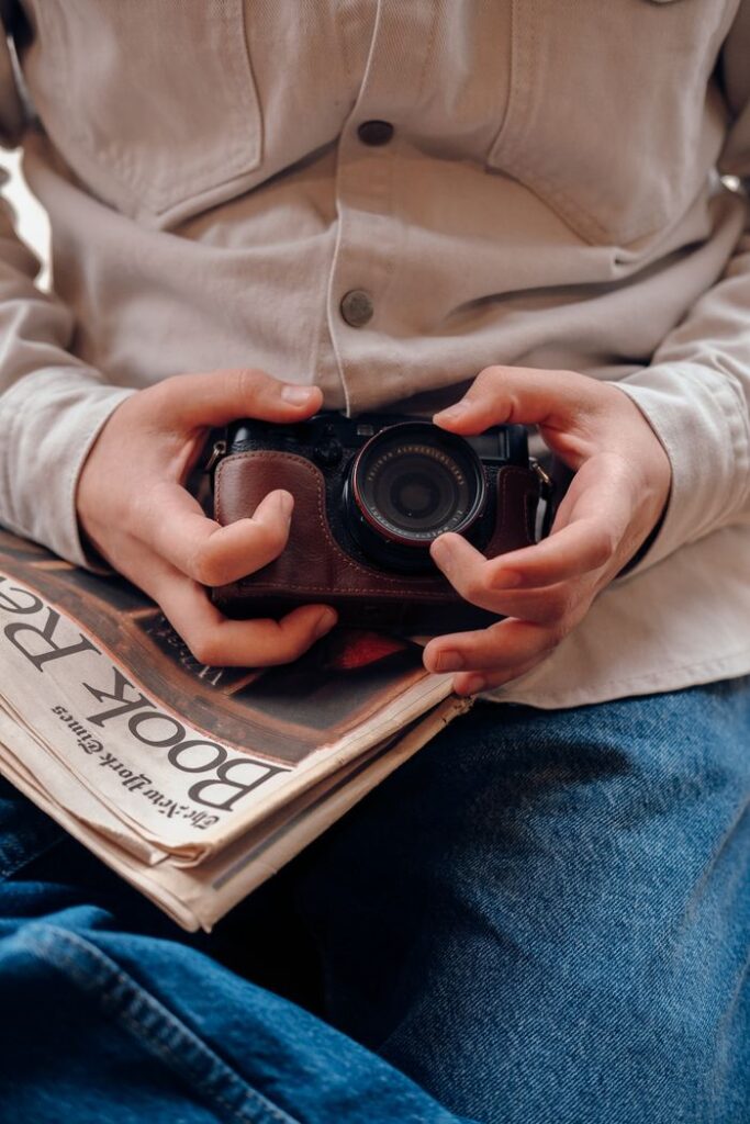 Close-up of hands holding a vintage camera and newspaper, evoking a retro feel.