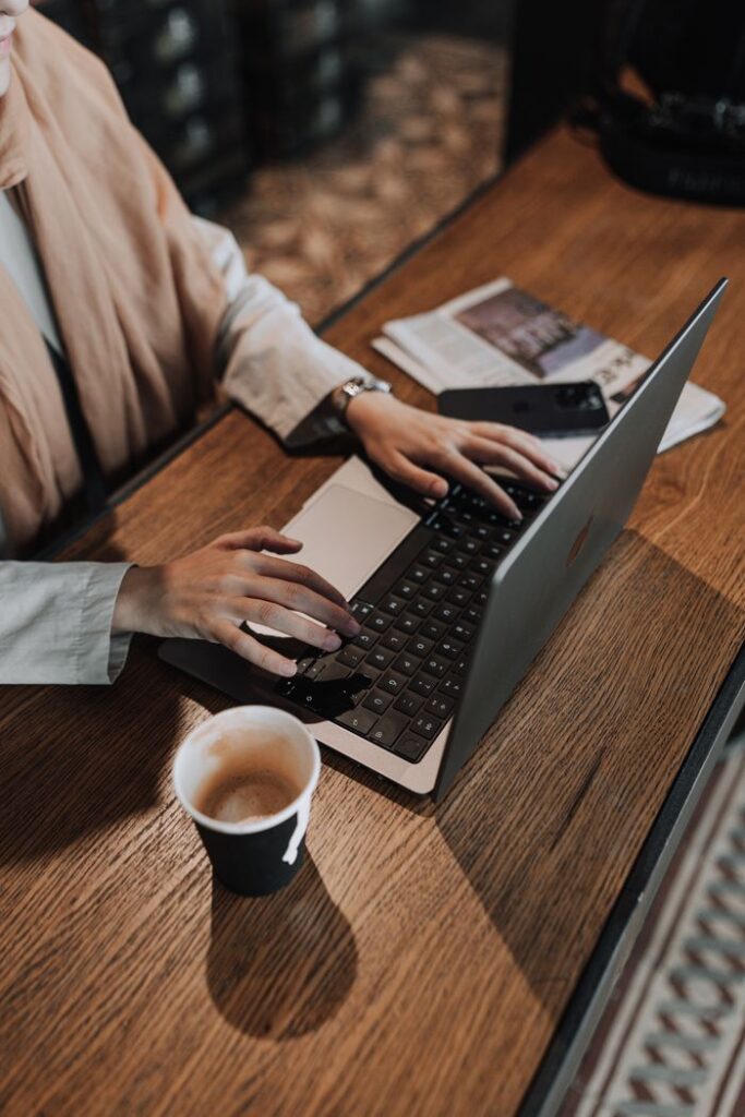 Female hands typing on laptop with coffee and newspaper nearby. Cozy workspace.
