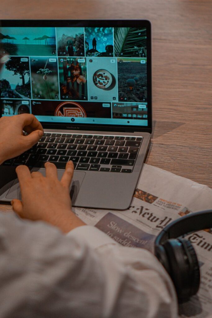 Close-up of hands working on a laptop browsing photos, with headset nearby.