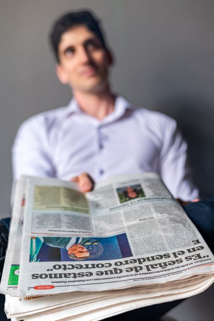 Close-up of a man holding a Spanish language newspaper, blurred background.